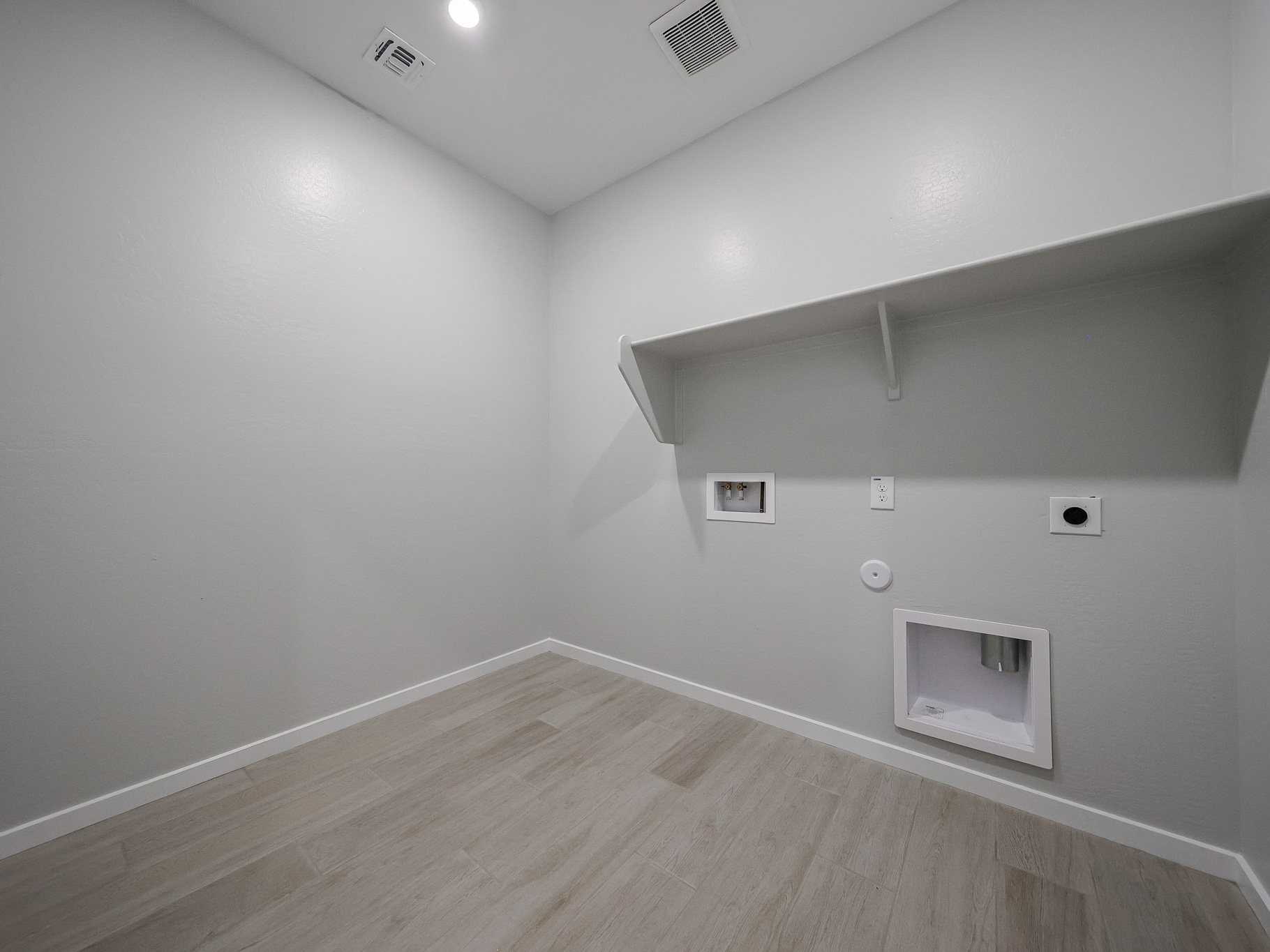 A room with a wood floor and a white wall with a vent.
