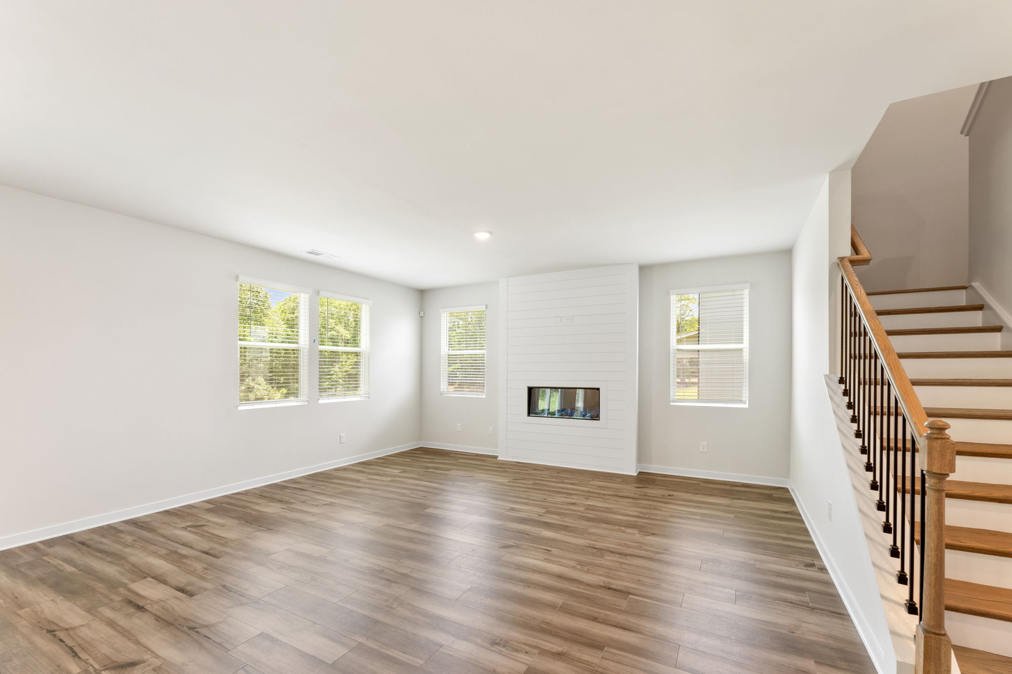 A large empty room with a wood floor and a staircase.