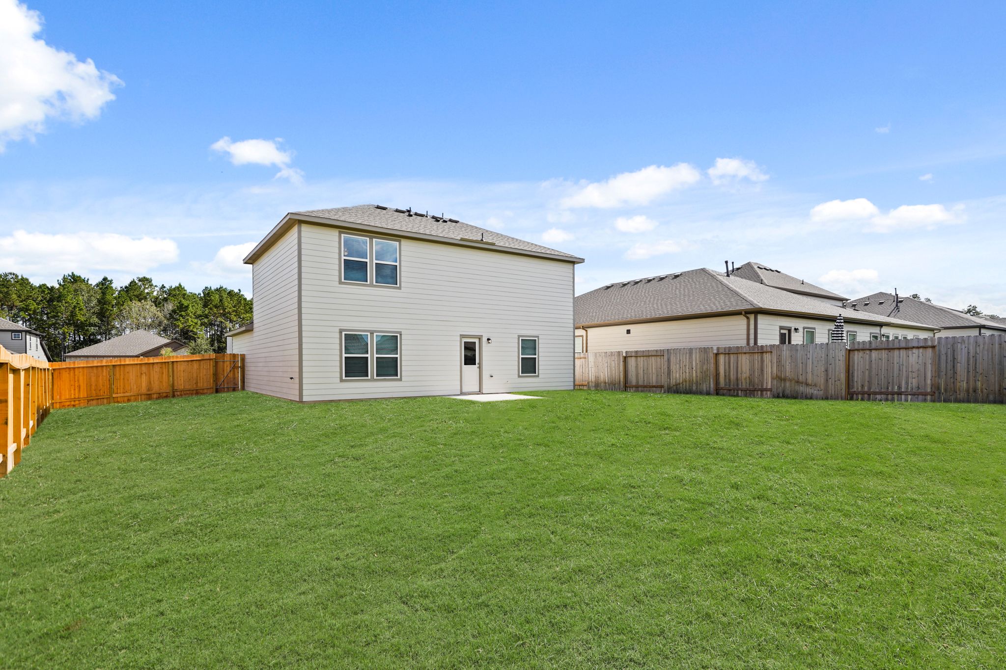 A large green lawn with a fence and a house in the background.