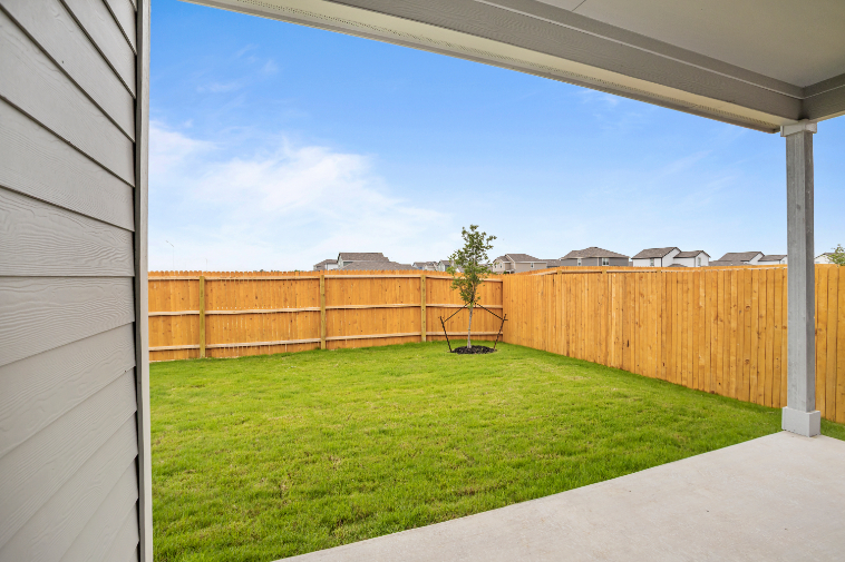 A fenced in yard with a tree and a house in the background.